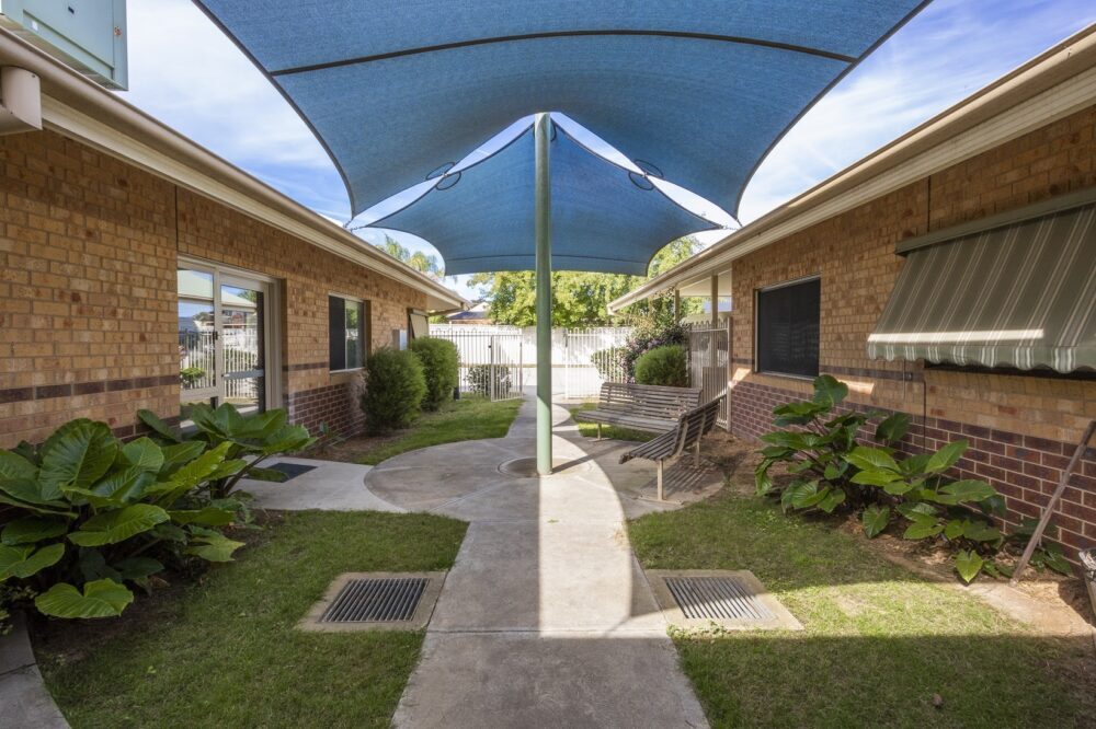 Garden area with large leafy plants under blue outdoor sails