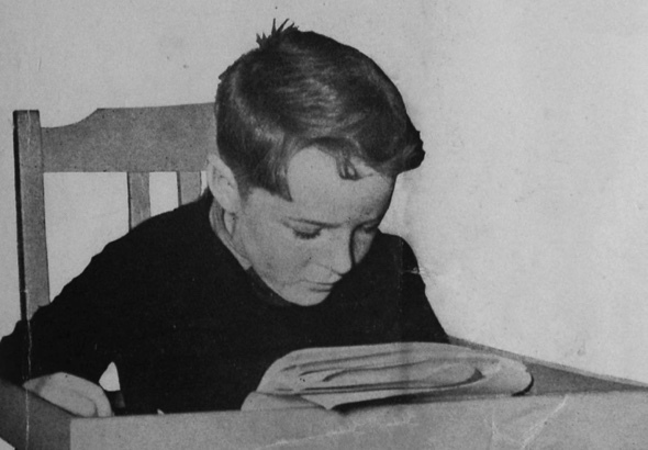Black and white image of boy reading the paper.