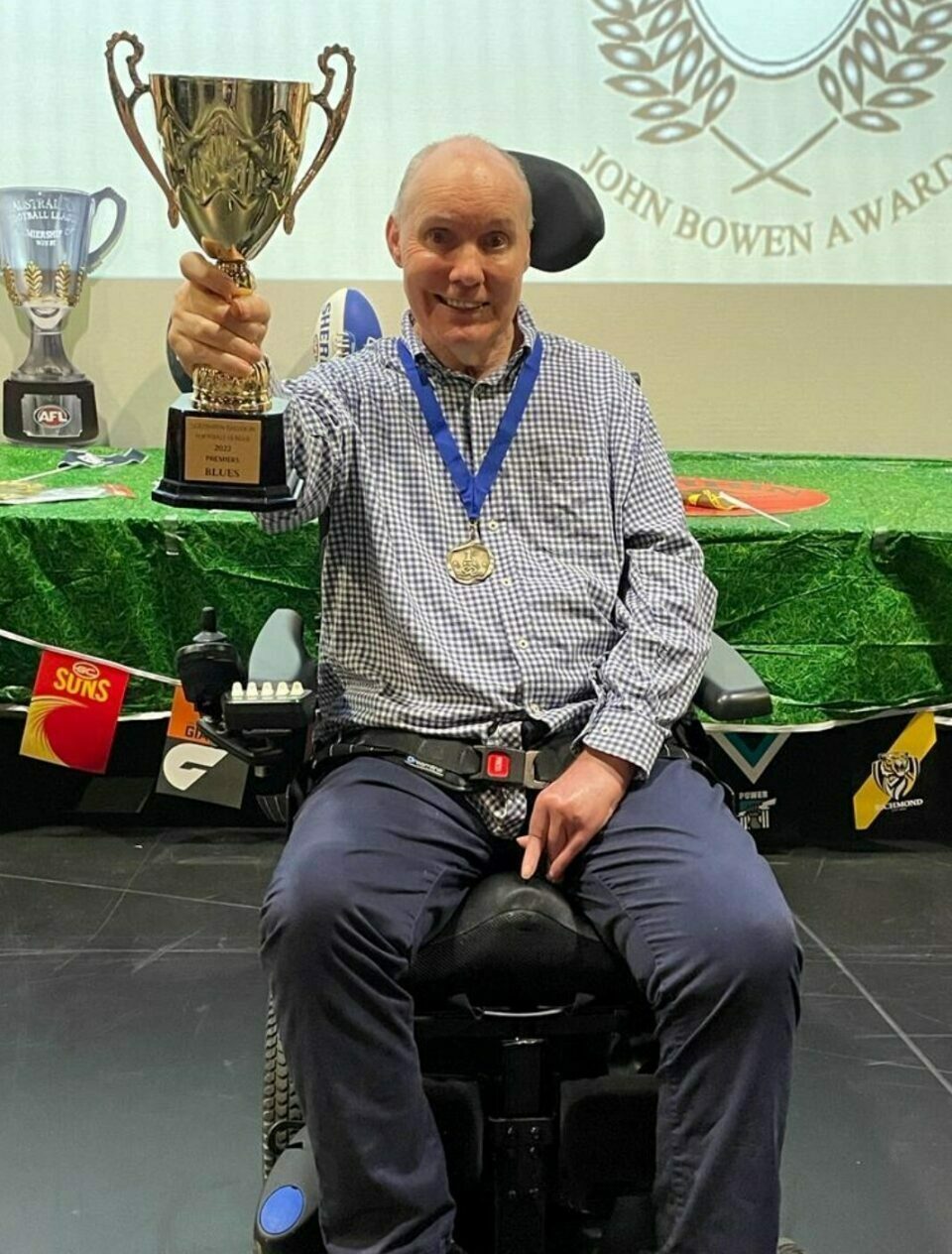 A man sitting on a wheelchair holding a gold trophy cup and medal.