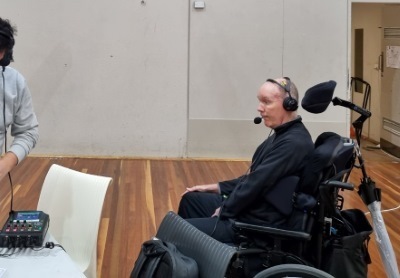 A man in the wheelchairs with a headset with mic