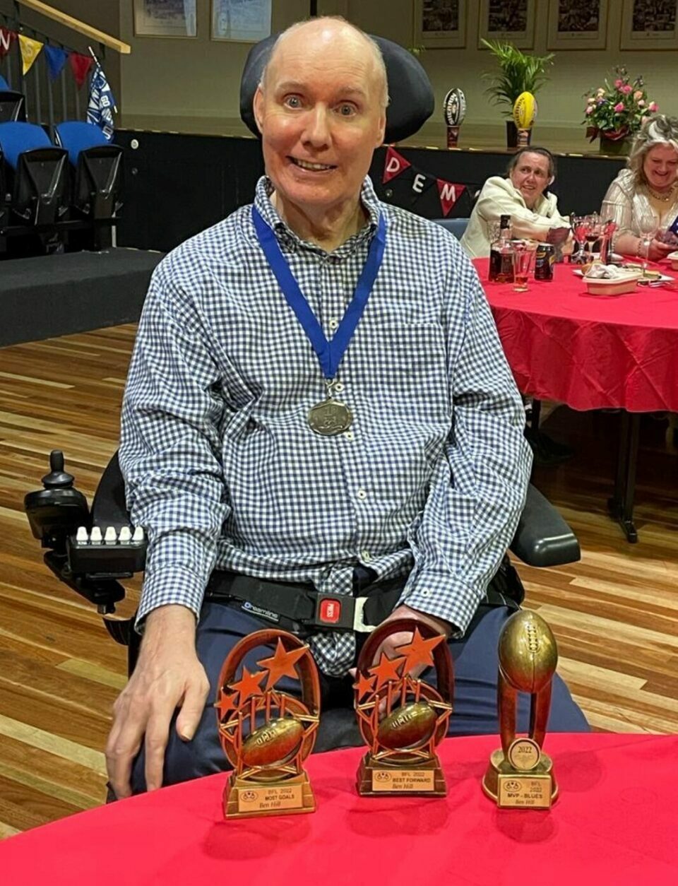 A man in the wheelchair with 3 award trophies.