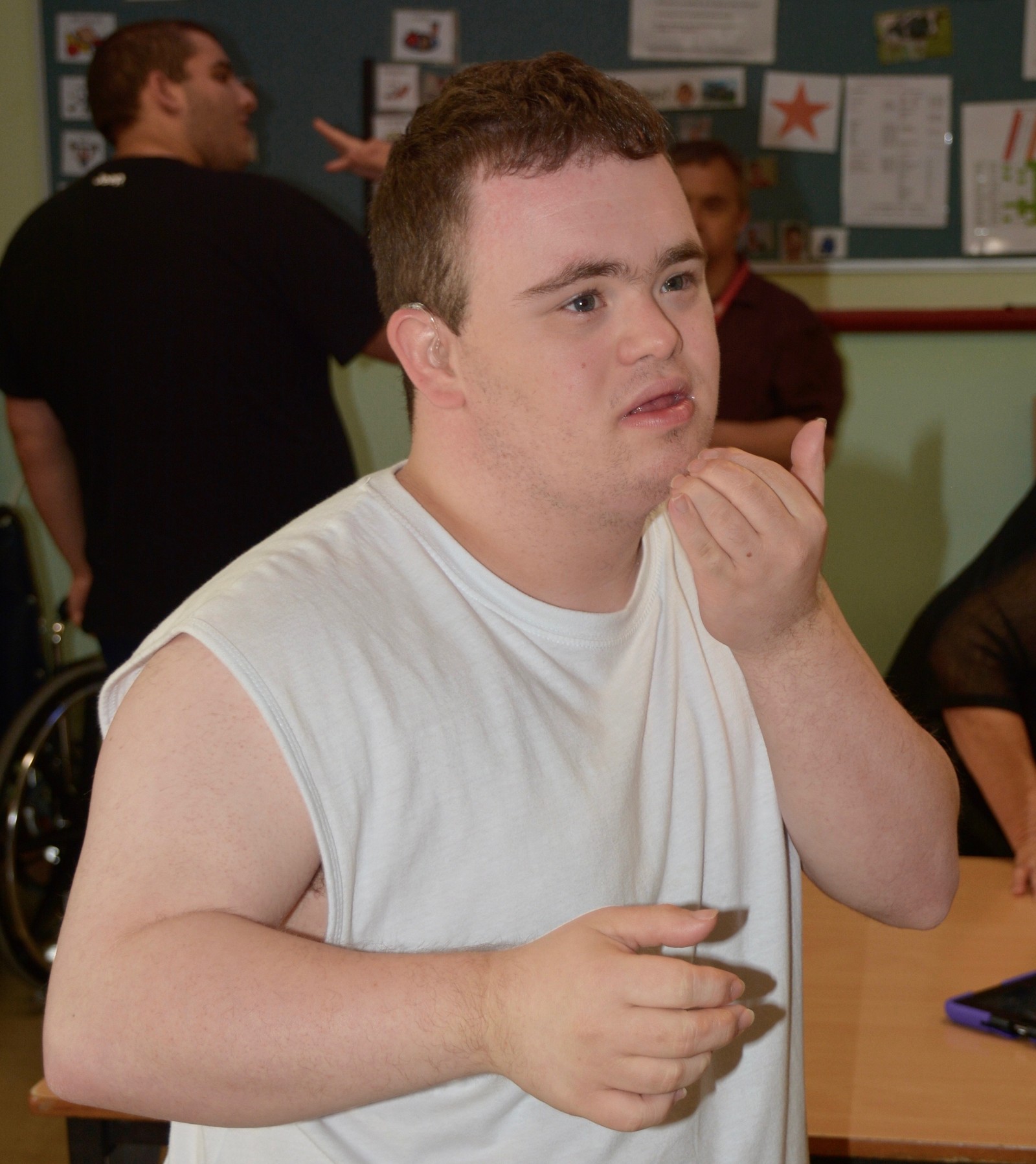 A boy wearing a white top is learning Key Word Sign