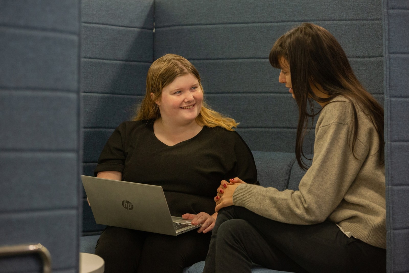 2 ladies are talking with each other with a laptop with them