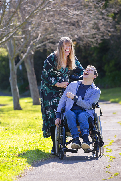 Scope participant in wheelchair, getting pushed along path by support worker.