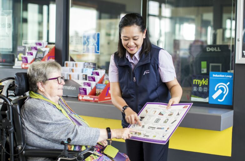 V Line employee using a communication board to talk with lady in a wheelchair.