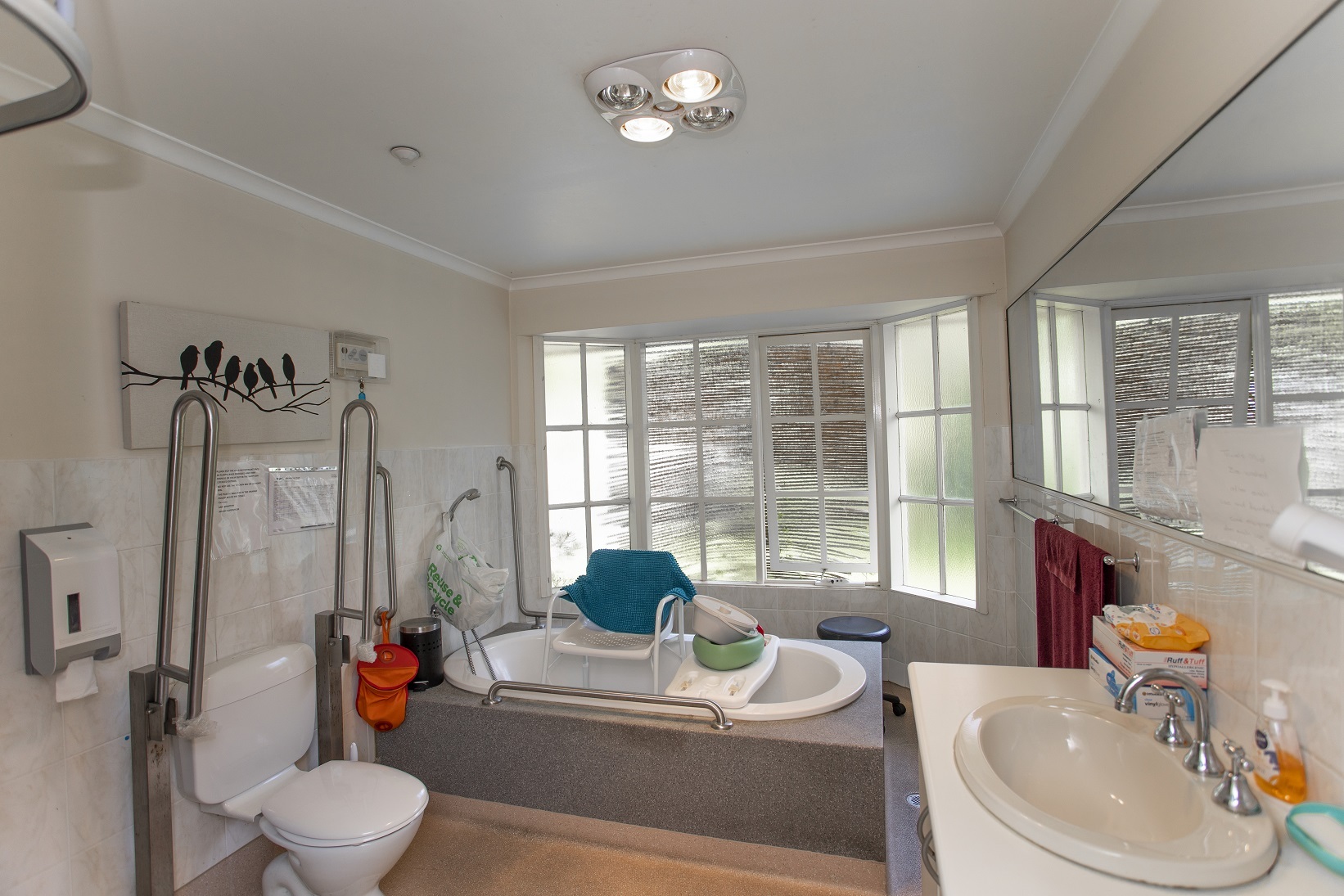 Well lit bathroom with bath and toilet that have grab rails