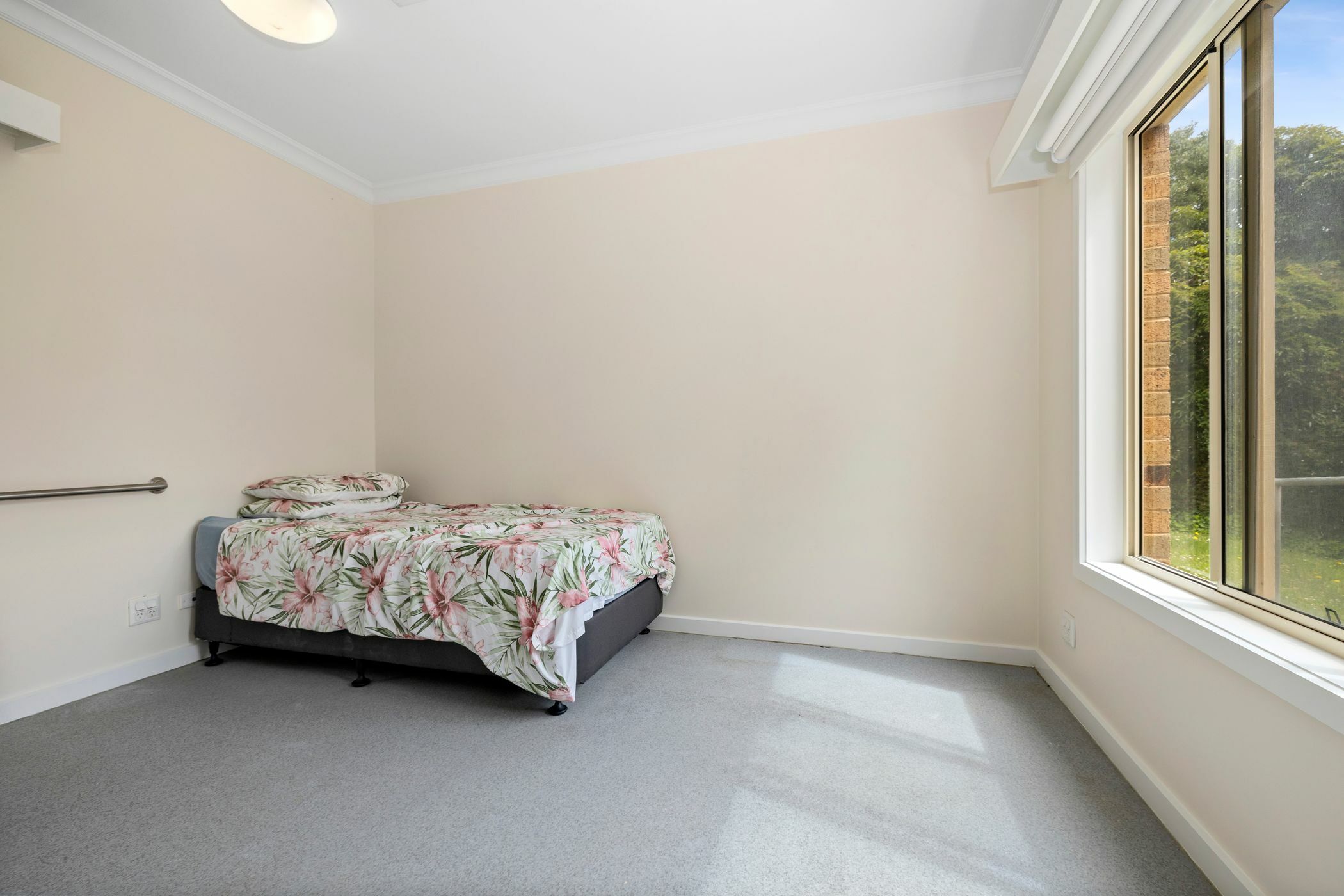 Well lit Bedroom with handrail and window looking out to yard